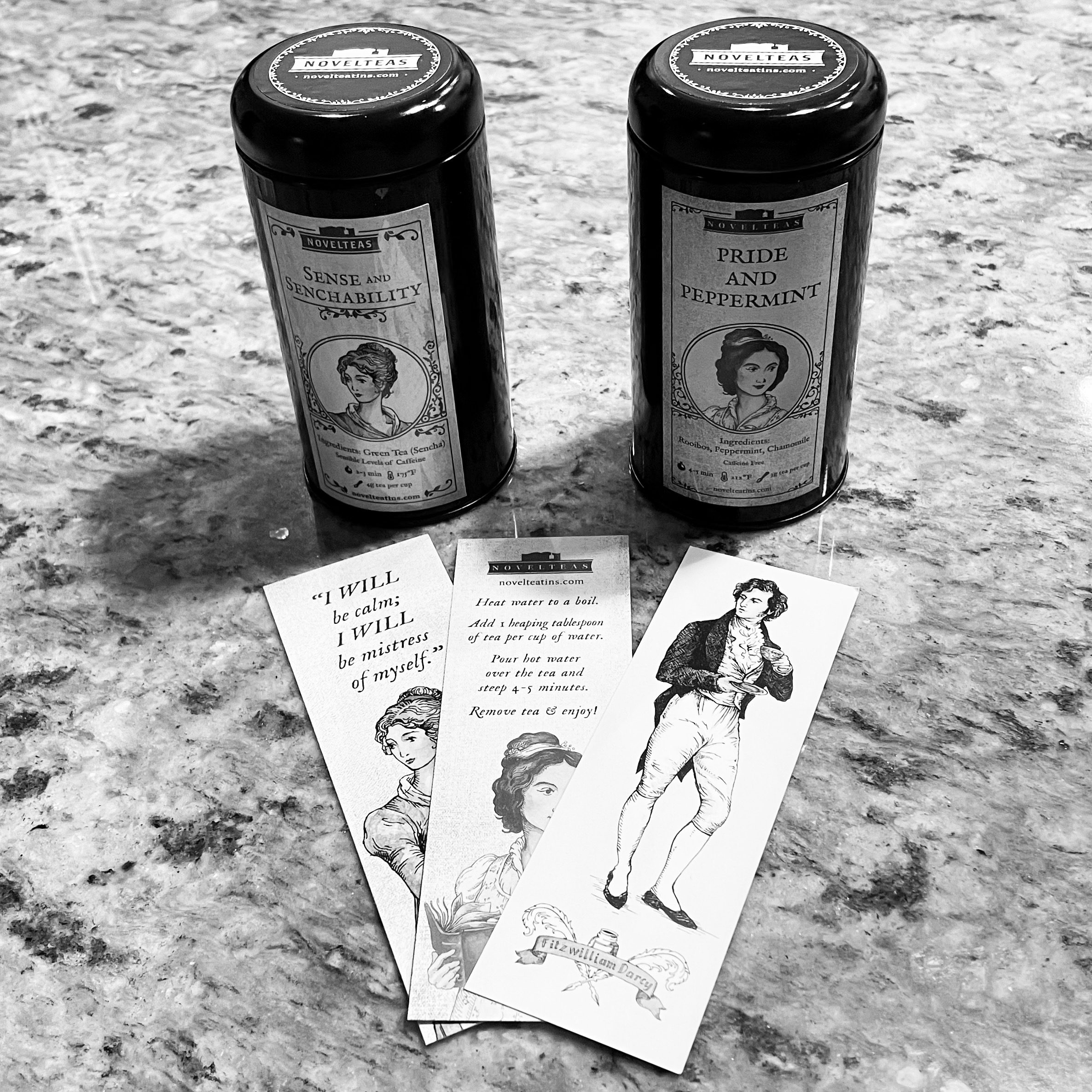 black and white photo with the two cylindrical tins of teas with three bookmarks with Jane Austen characters fanned out in front